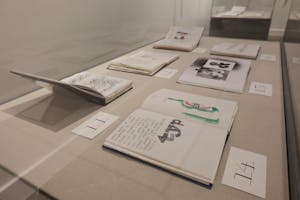 Photo of a series of sketchbooks on display in a clear case, each opened to drawings and numbered on a placard below.