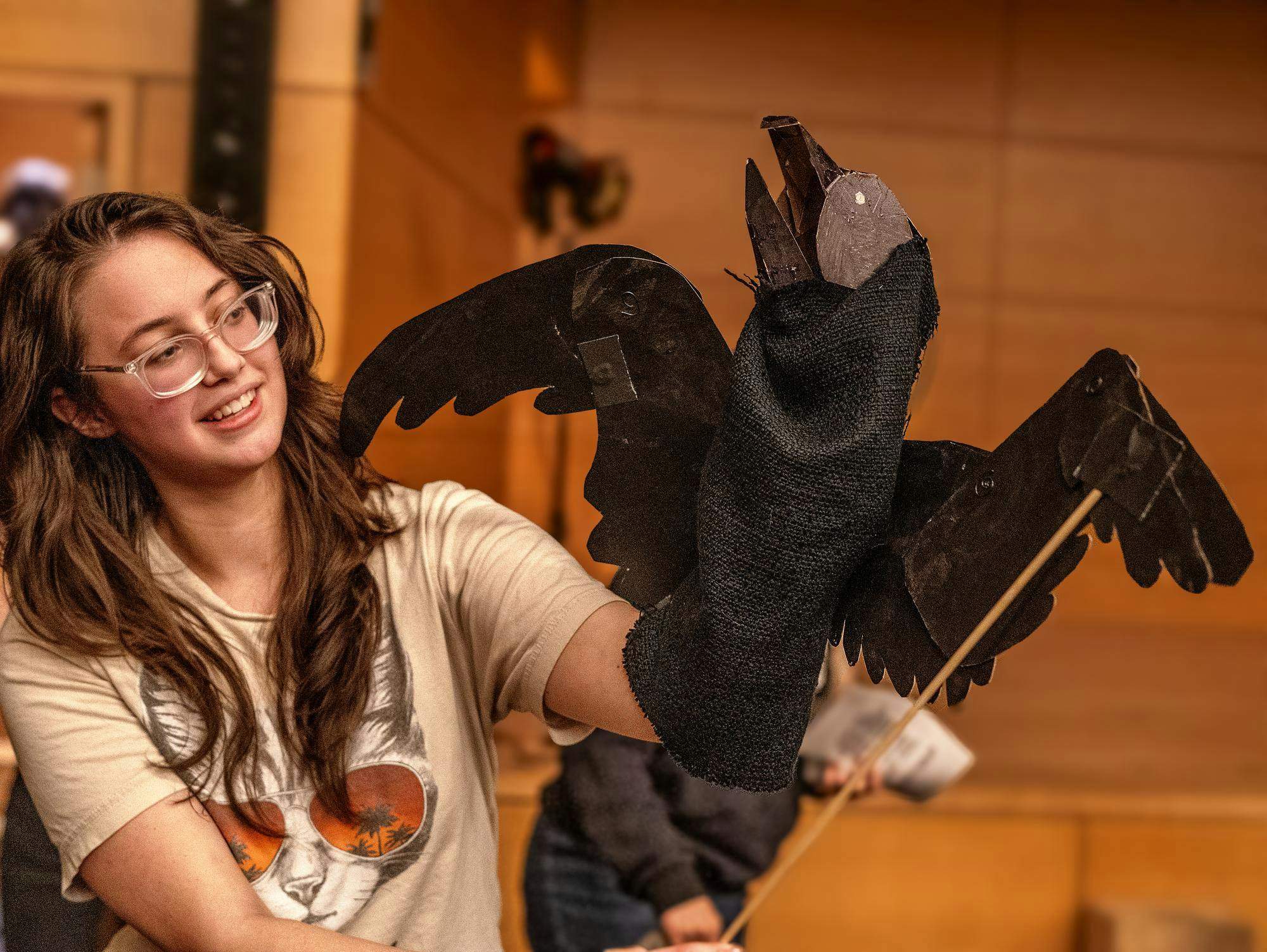 Girl with classes holds mixed media black puppet. 