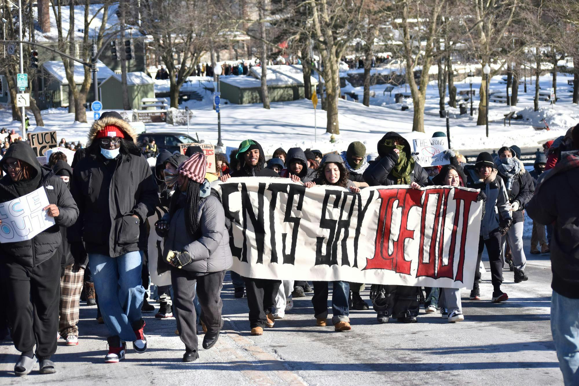 A group of people march to the State House holding a sign that reads: “Ice Out.”