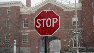 Photo of a stop sign with snow falling around it. The sign is in front of a red brick building.


