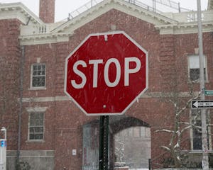 Photo of a stop sign with snow falling around it. The sign is in front of a red brick building.