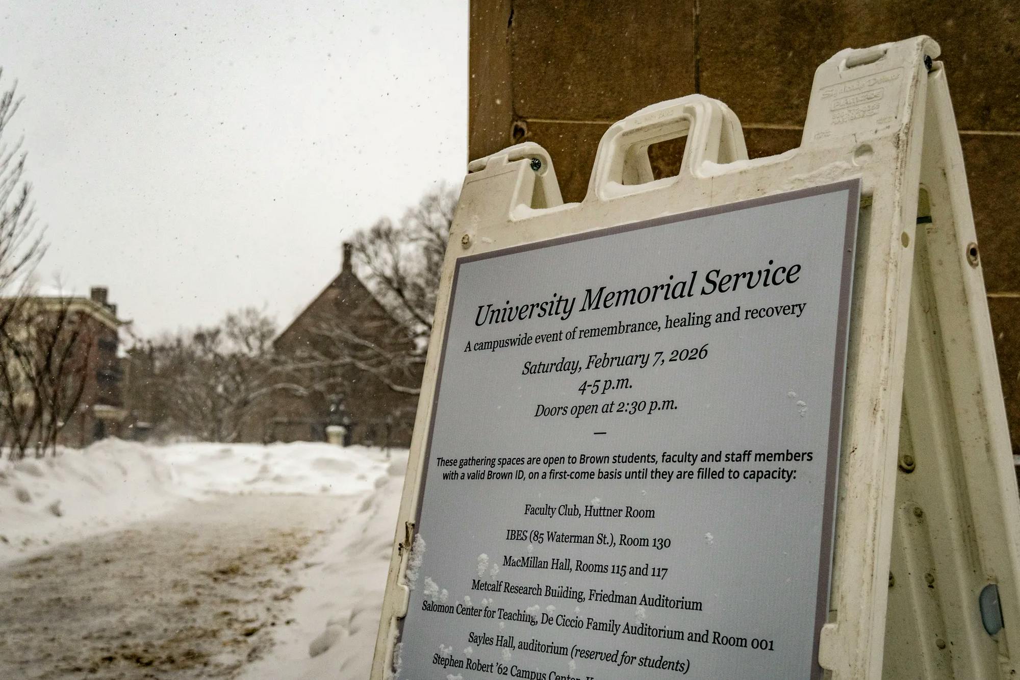 The photo shows a sign for the memorial service outlining the various locations for live viewing. Sayles Hall is pictured in the background to the left. 
