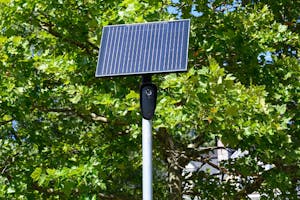 Photo of a black security camera with a solar panel on top of a white pole.