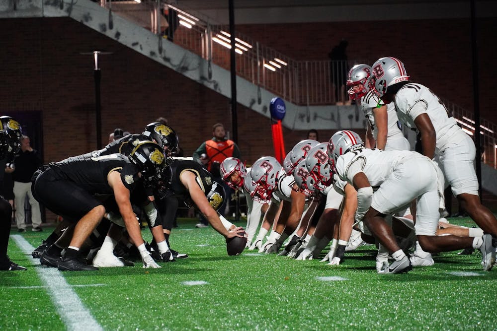 Photo of Brown and Bryant football players face to face at the start of a play, as Bryant holds the ball.