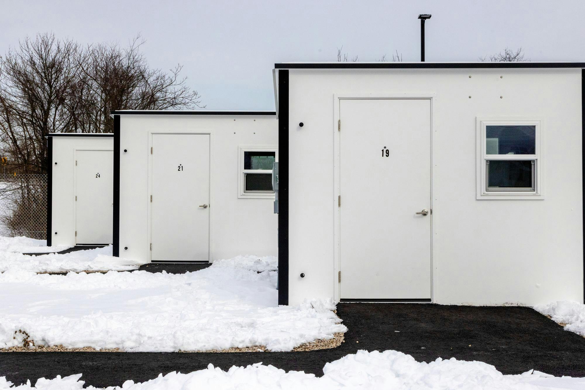 A row of three white pallet shelters in echo village. Snow carpets the ground.