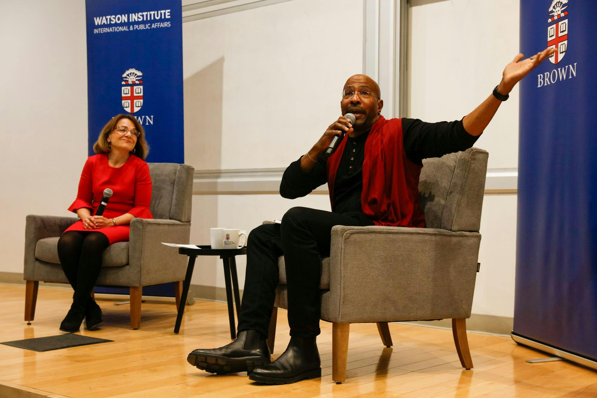 A picture of CNN host Van Jones, wearing a black shirt and red tie, on stage and speaking into a microphone.