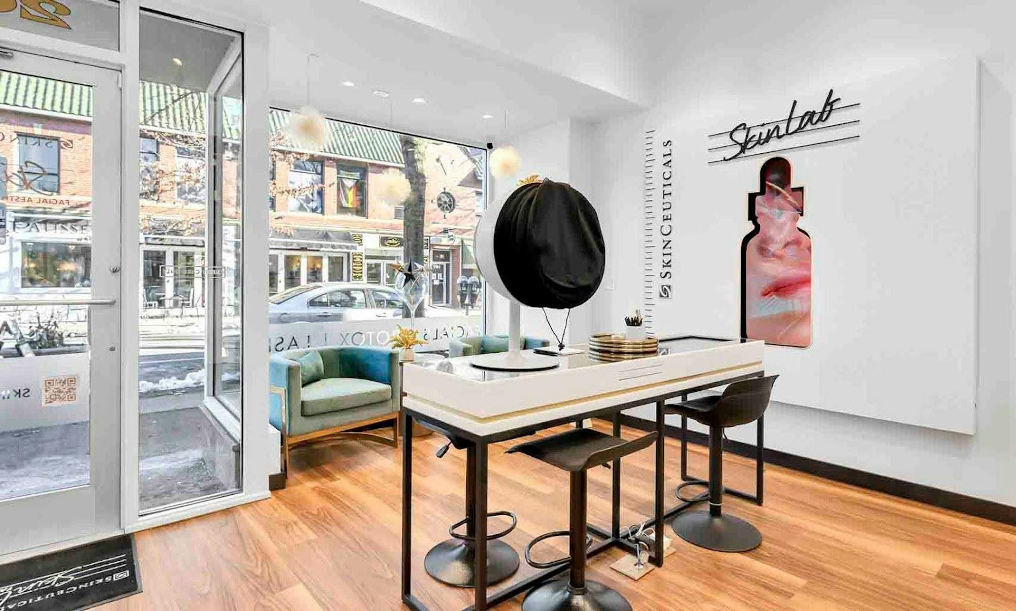 A picture of the SkinCeuticals SkinLab in Providence. There is a counter with several bar stools gathered around. There are also lounge chairs and a large sign that says "Skinlab."