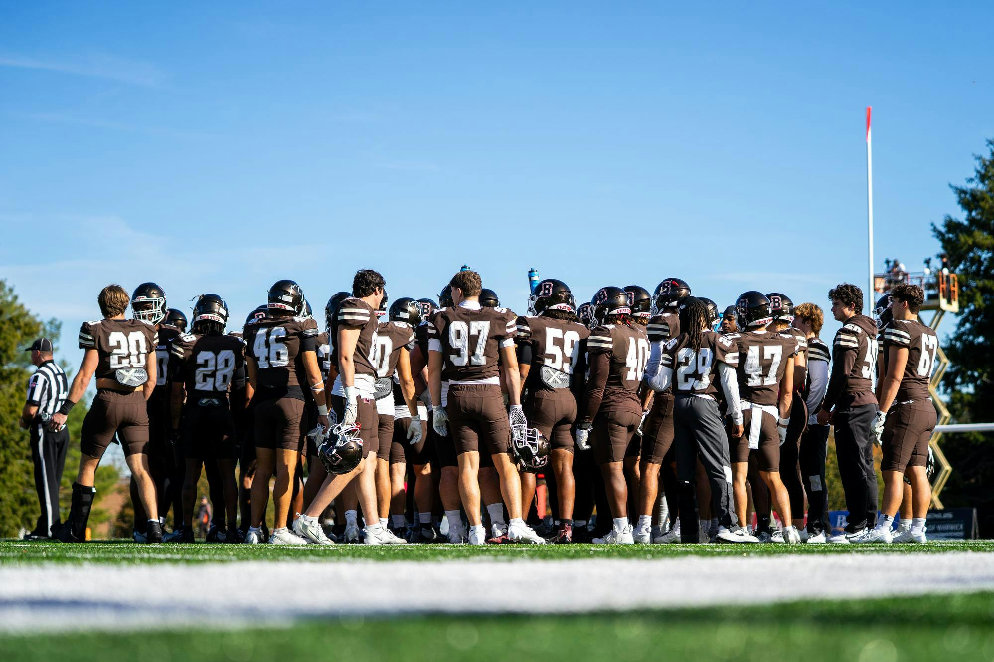 Brown football players standing in a huddle on the football field