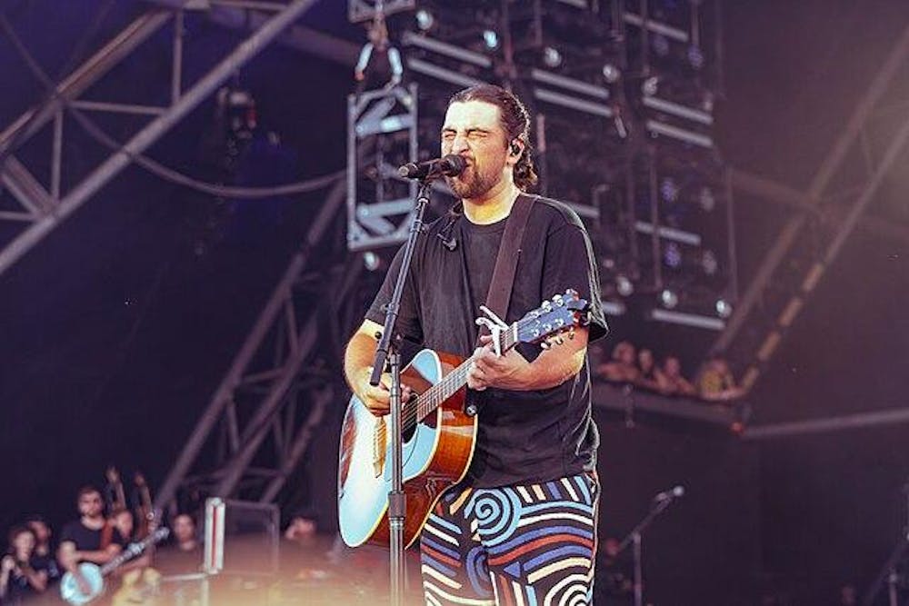 Noah Kahan sings into the microphone while playing the acoustic guitar.
