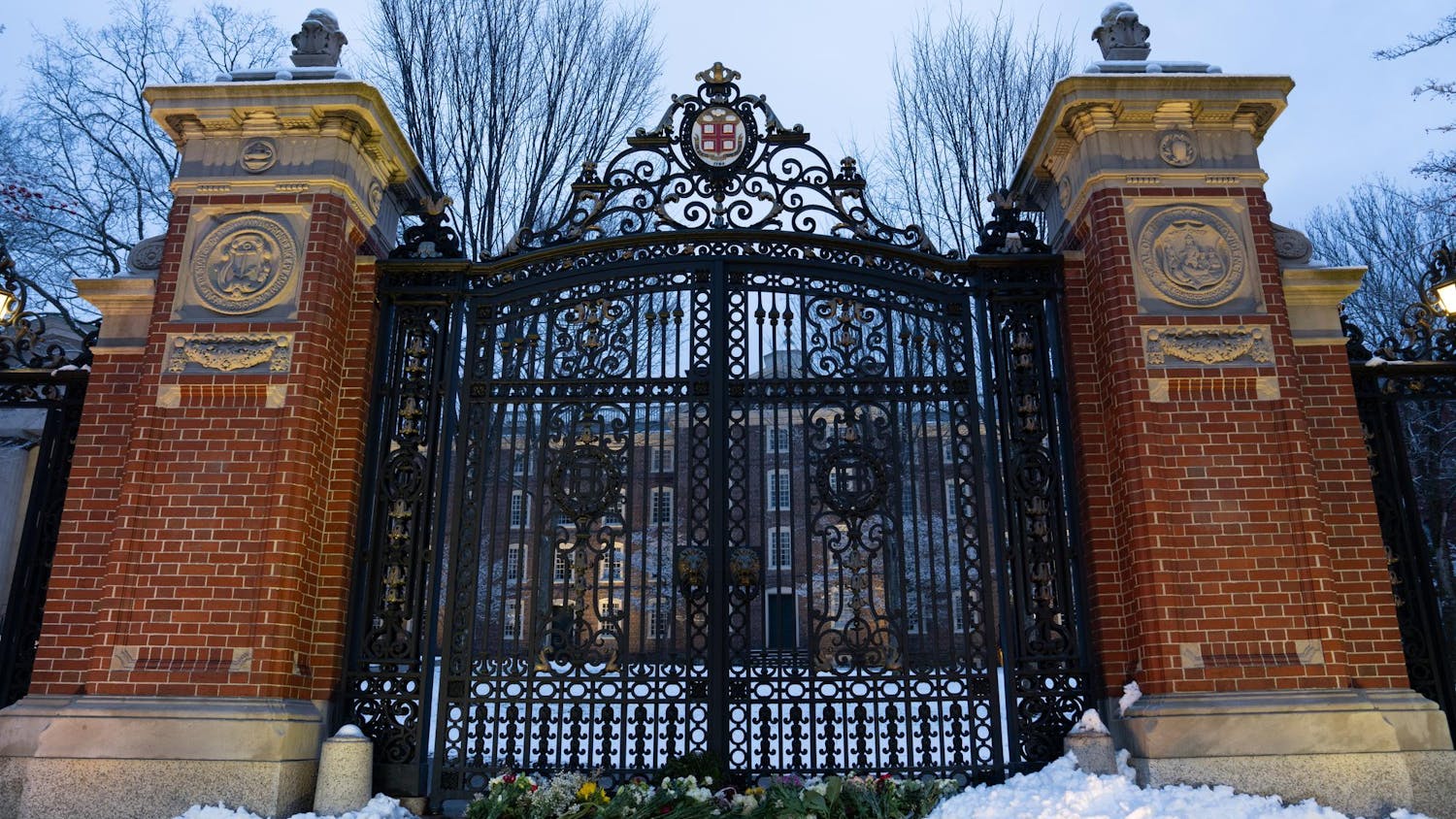 A photo of the Van Wickle Gates with snow and flowers at the bottom of the gates.