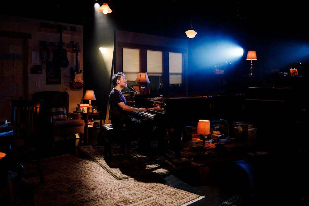 Image of Gabriel Kahane playing the piano while singing in a dark room.