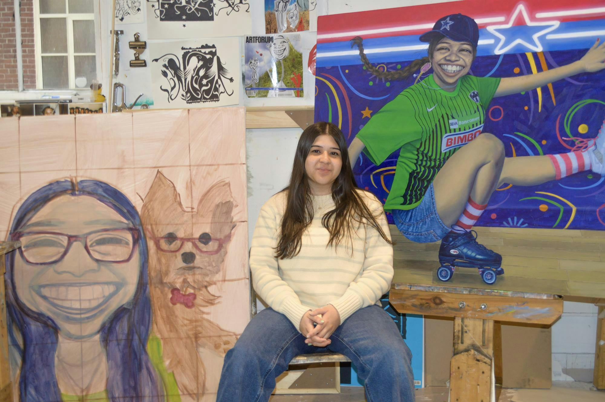 Camila Salinas sits in front of a number of her paintings. 