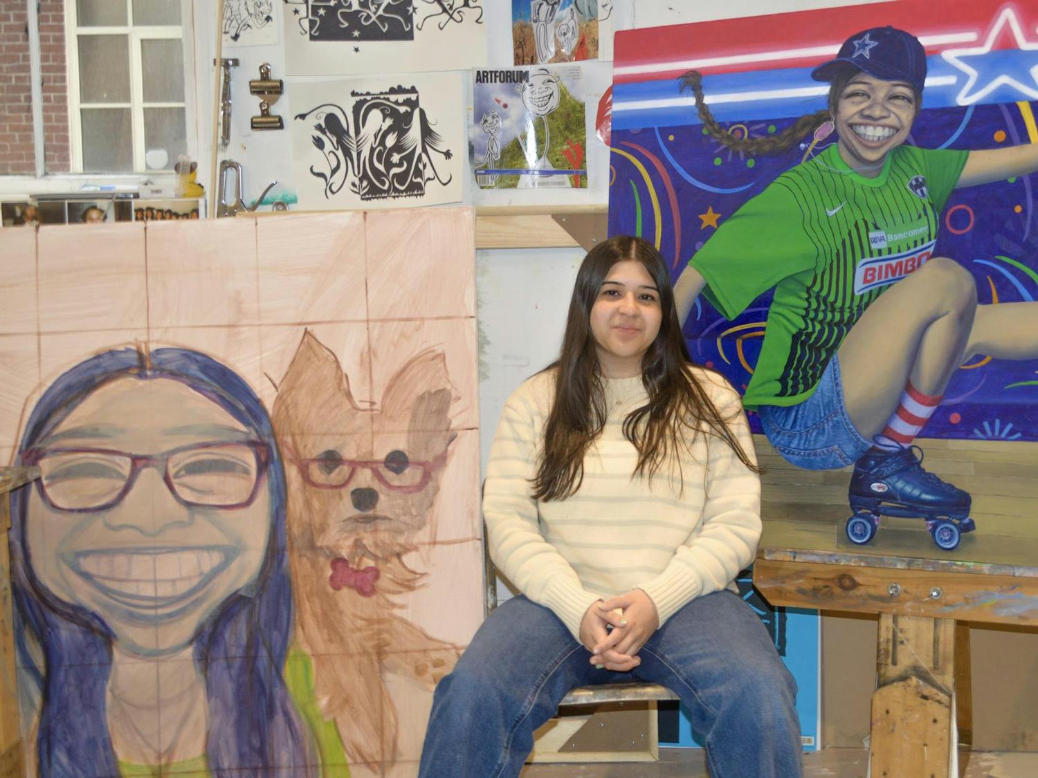 Camila Salinas sits in front of a number of her paintings.