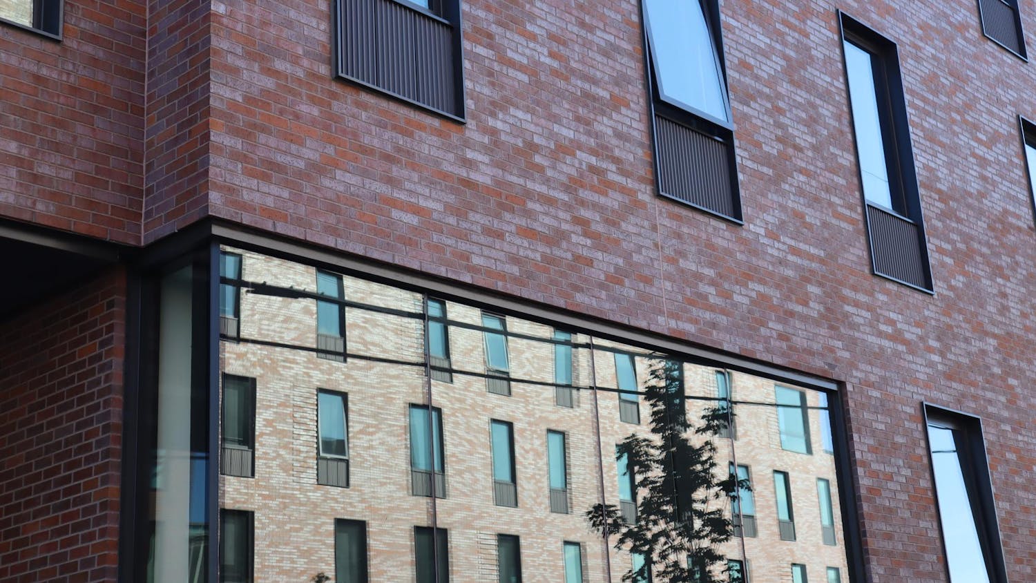 Close image of a Brown University dorm exterior. It is a brick building with another brick building reflected in a large window.