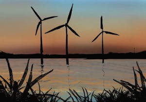 Three windmills stand in a body of water with a sunset in the background. 