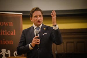 A photo of Rep. Dean Phillips at Brown University Sayles Hall speaking into a microphone with his hand up.