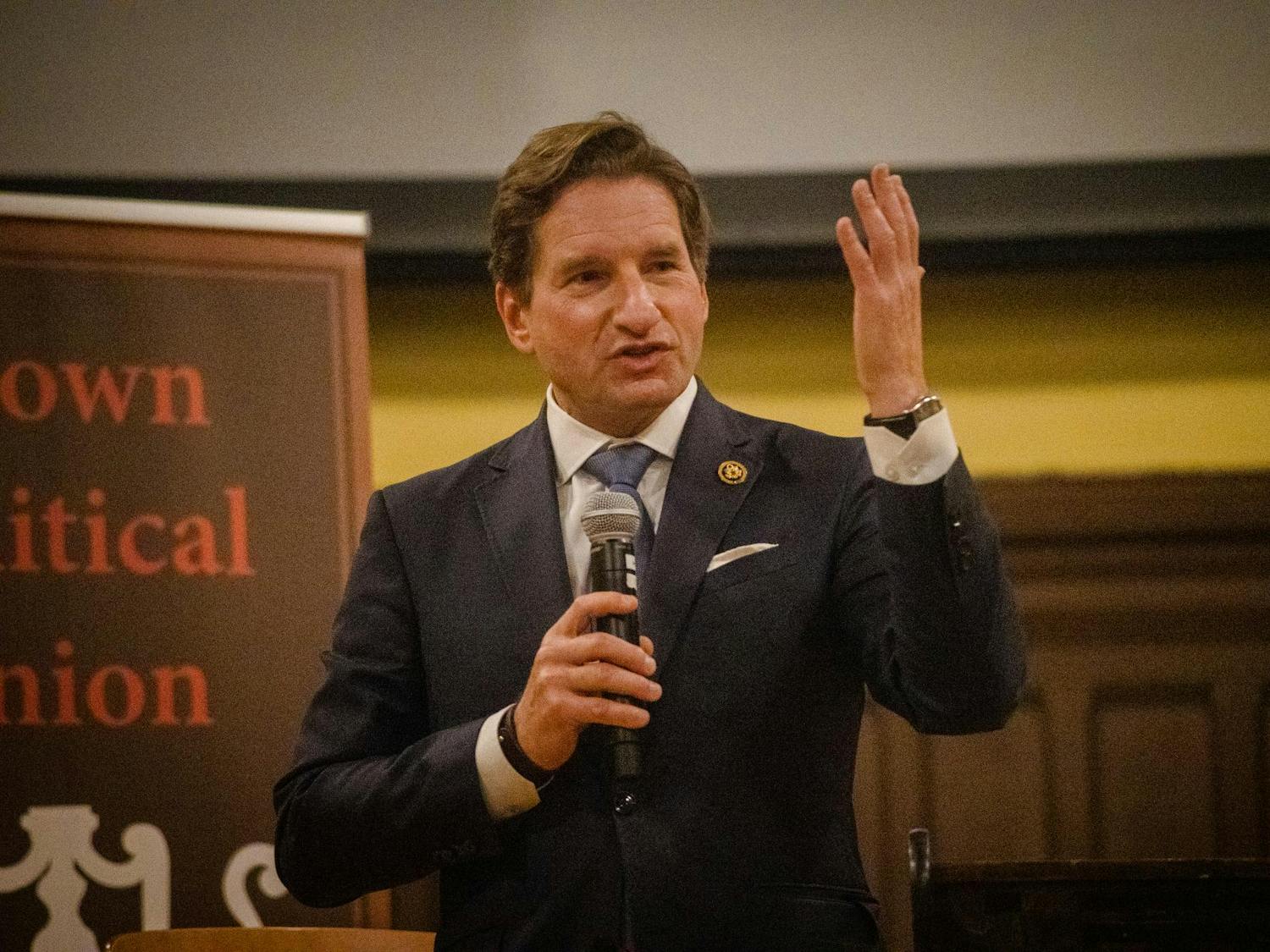 A photo of Rep. Dean Phillips at Brown University Sayles Hall speaking into a microphone with his hand up.