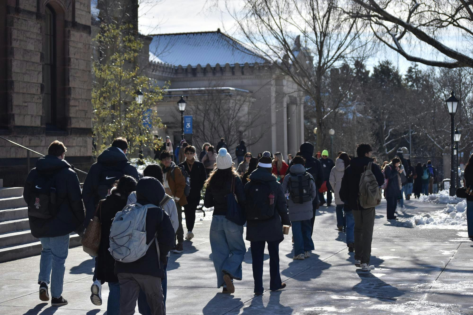 Students in winter clothes walk in front of Sayles Hall on a sunny, snowy day.
