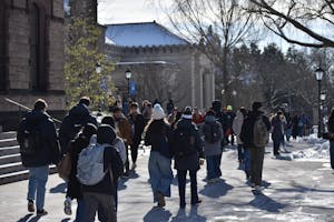 Students in winter clothes walk in front of Sayles Hall on a sunny, snowy day.
