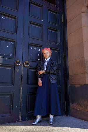 Photo of a graduate student with bright pink hair standing on the steps.