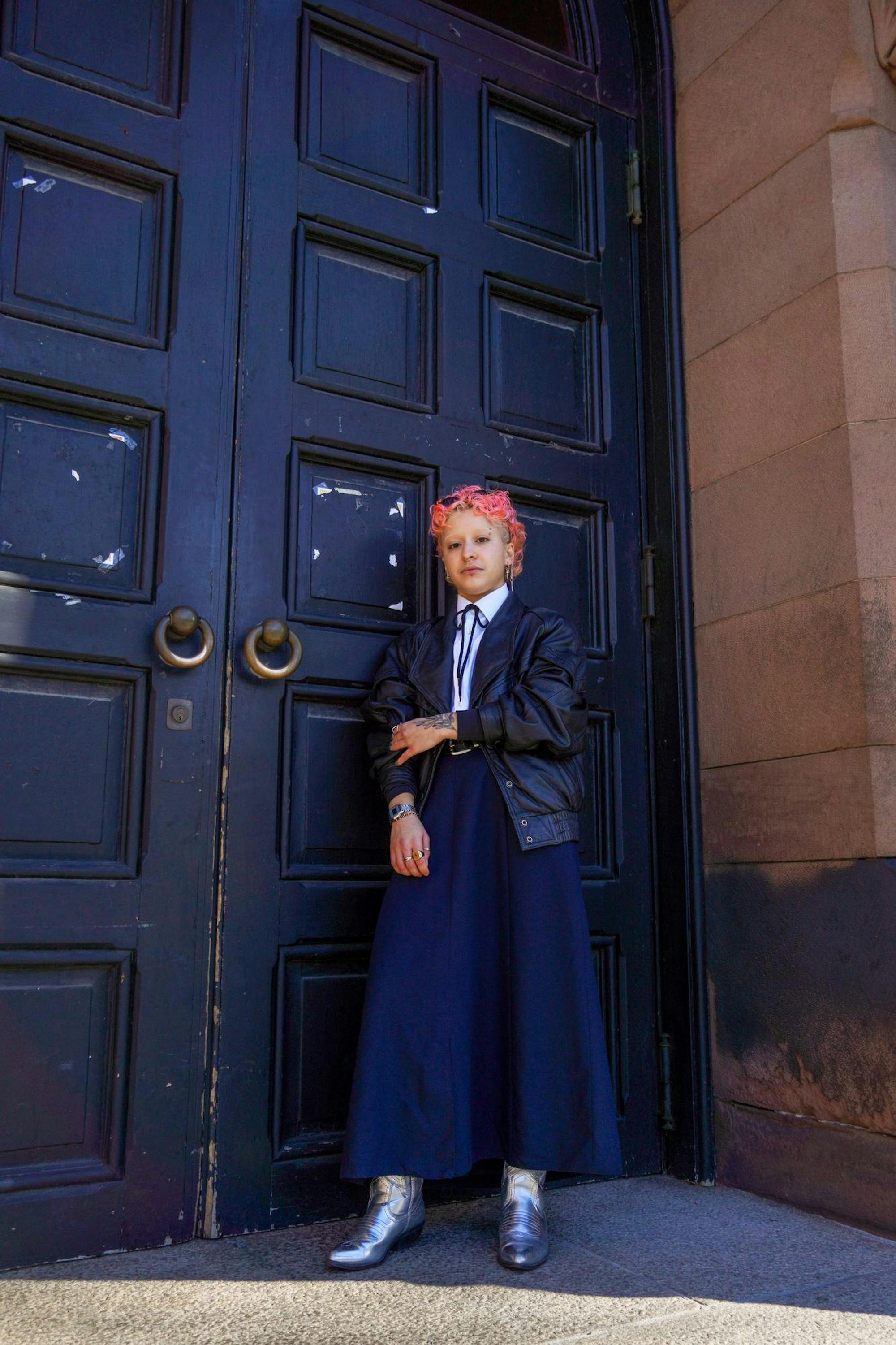 Photo of a graduate student with bright pink hair standing on the steps.