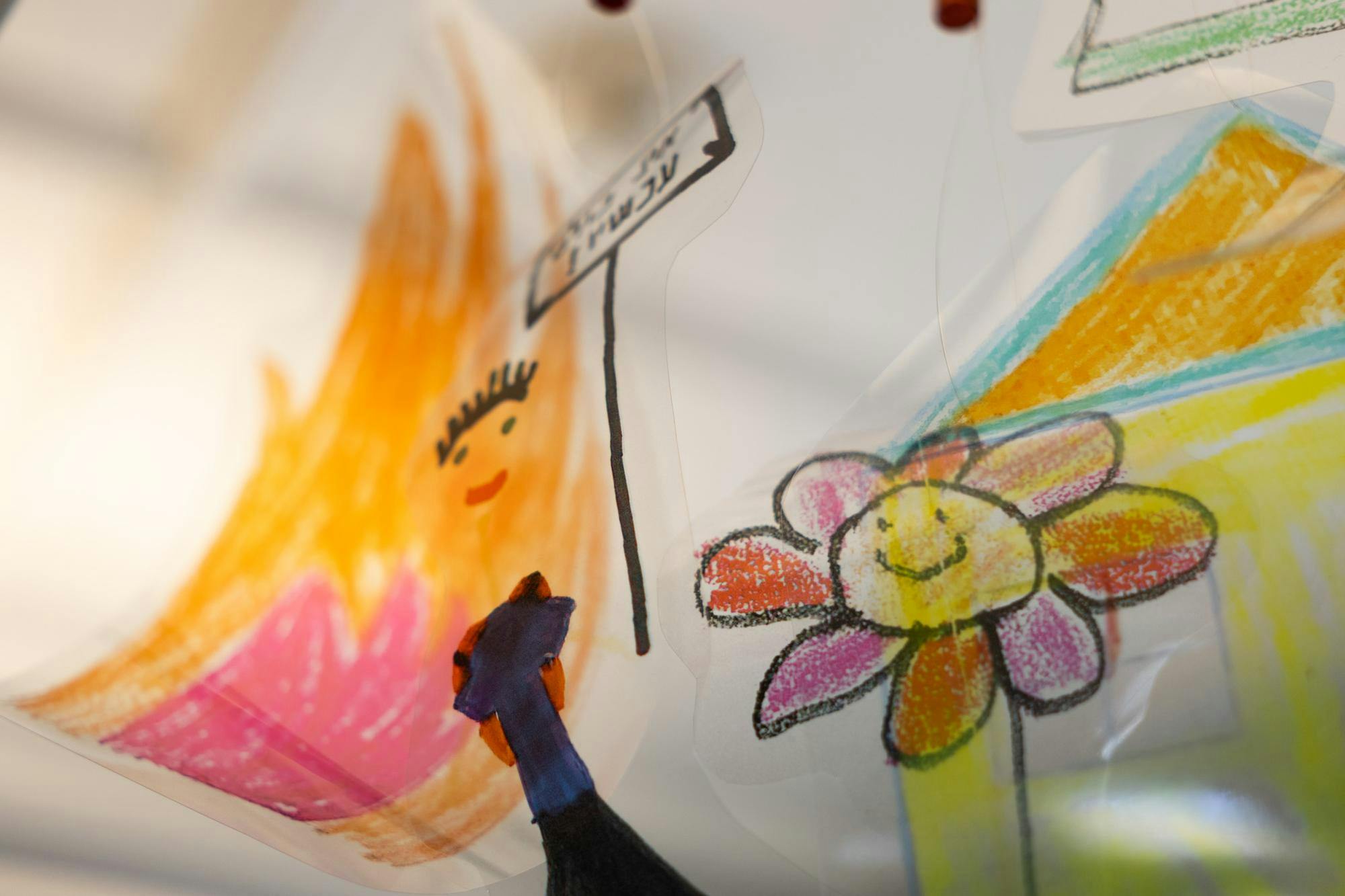 Photo of a child’s artwork depicting a flower and a person holding up a sign in front of a house.


