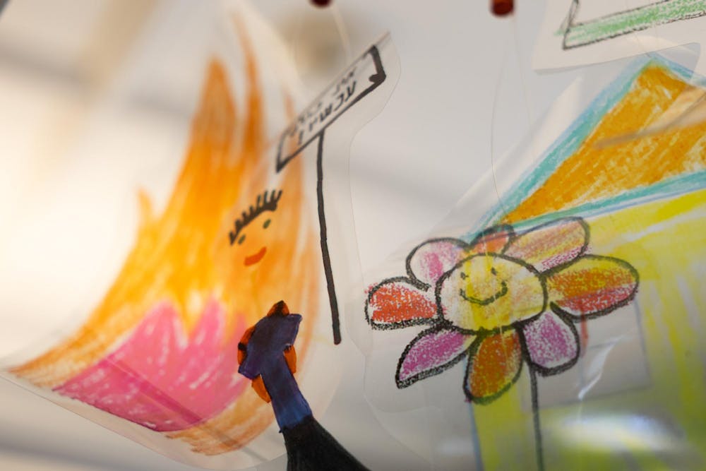 Photo of a child’s artwork depicting a flower and a person holding up a sign in front of a house.


