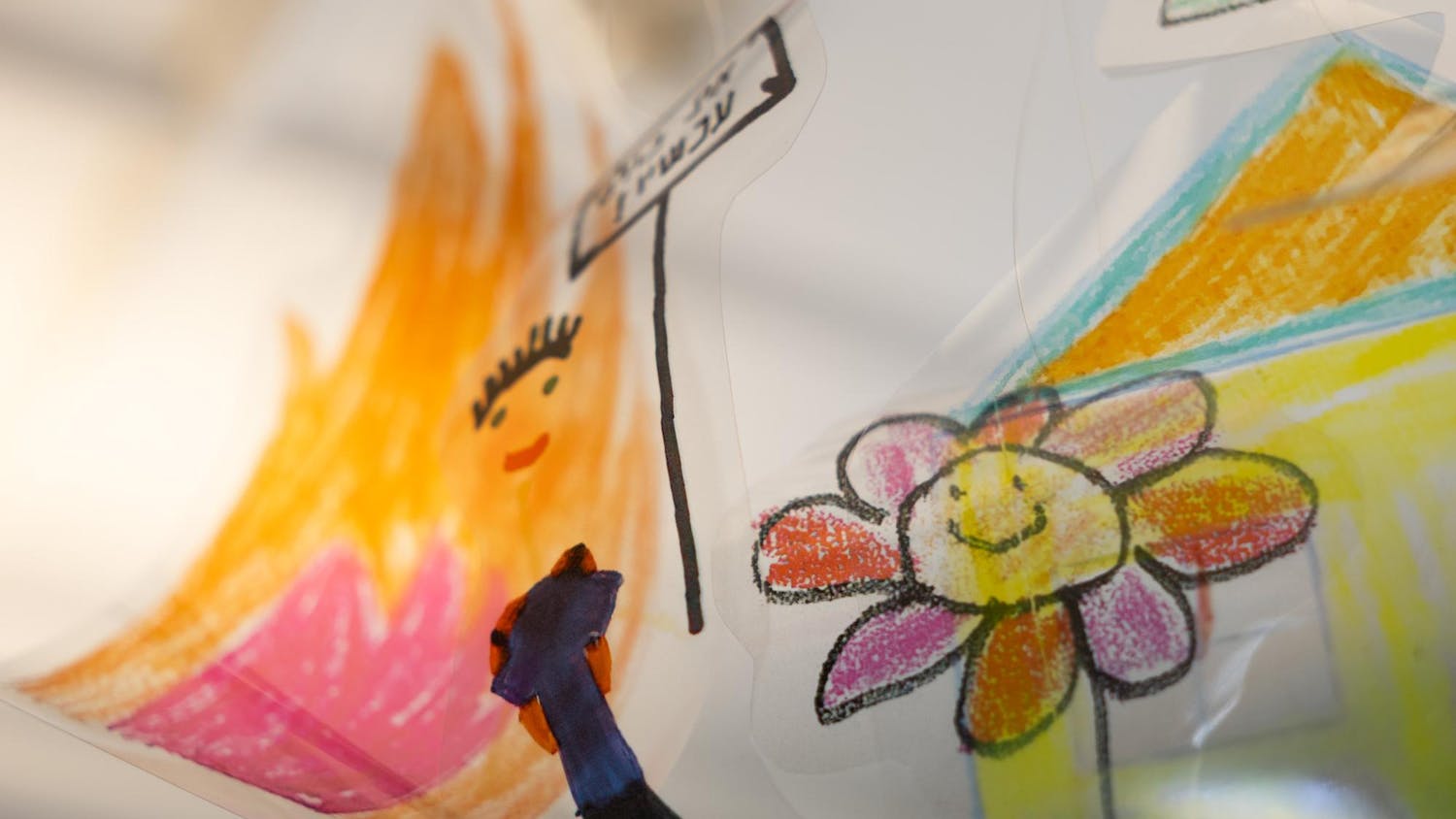 Photo of a child’s artwork depicting a flower and a person holding up a sign in front of a house.