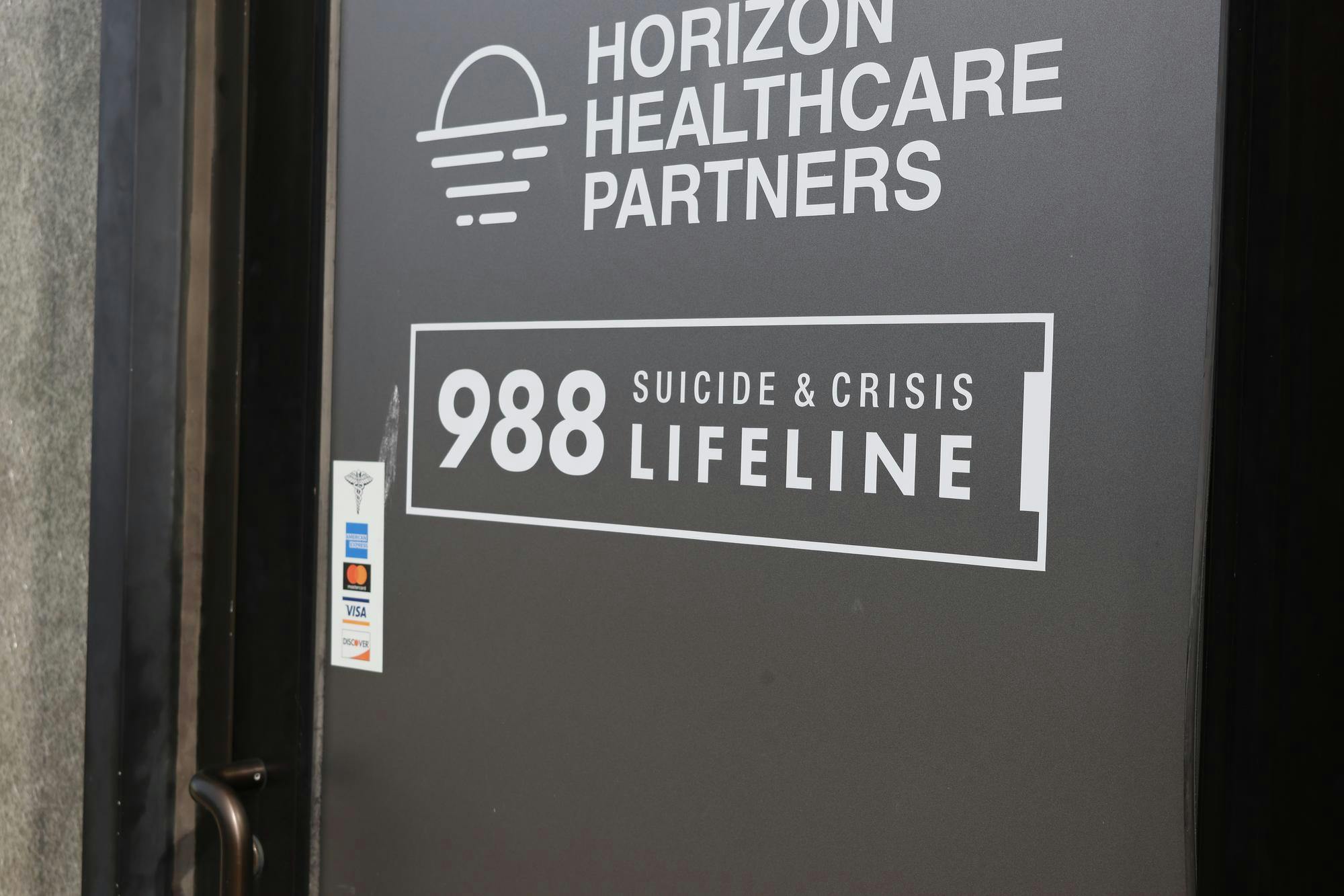 The door of Horizon Healthcare Partners, a behavioral health facility located in East Providence. The door reads "988 Suicide and Crisis Lifeline."