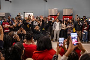 Photo of Brown students dancing in the Sharpe Refectory in a circle with students filming in front of two soda machines.