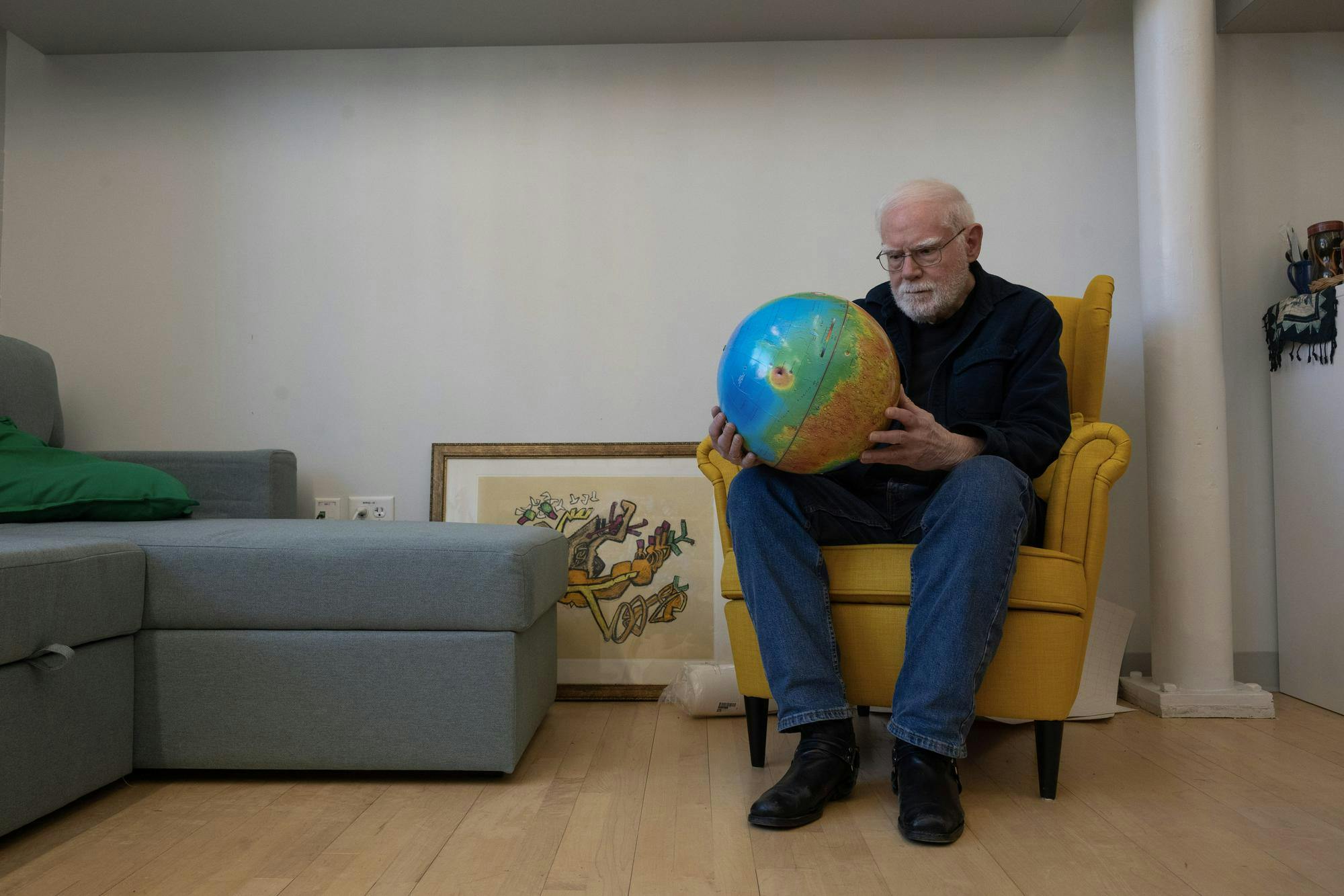 A photo of Professor James Head sitting on a chair and looking at a globe he is holding in his hands. 