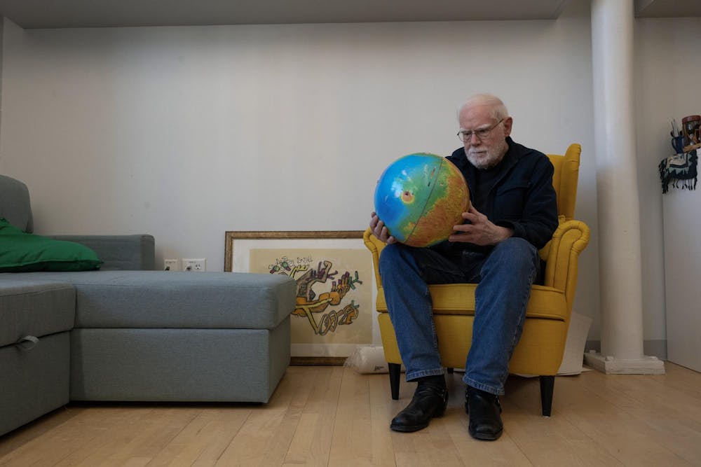 A photo of Professor James Head sitting on a chair and looking at a globe he is holding in his hands. 