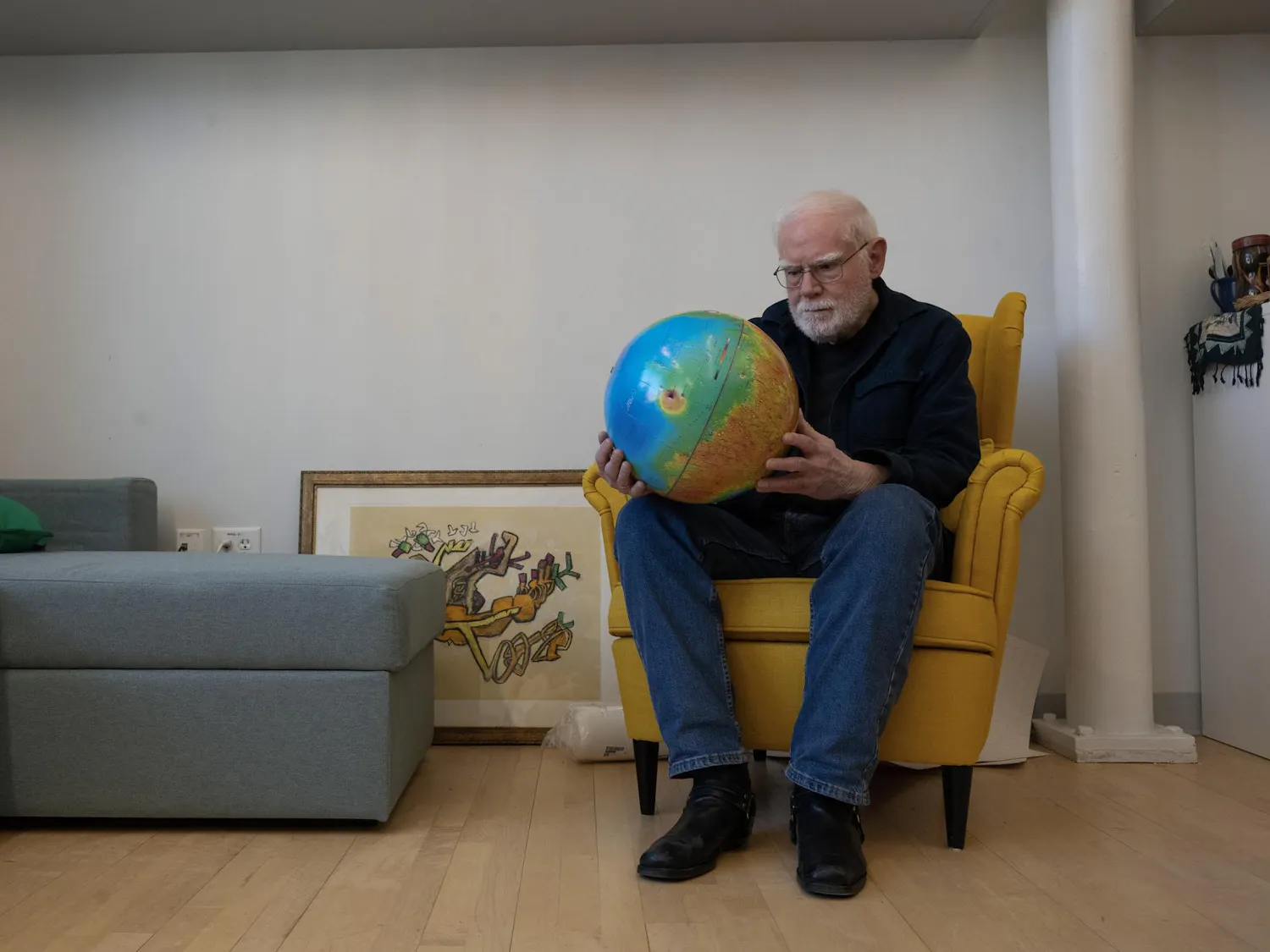 A photo of Professor James Head sitting on a chair and looking at a globe he is holding in his hands.