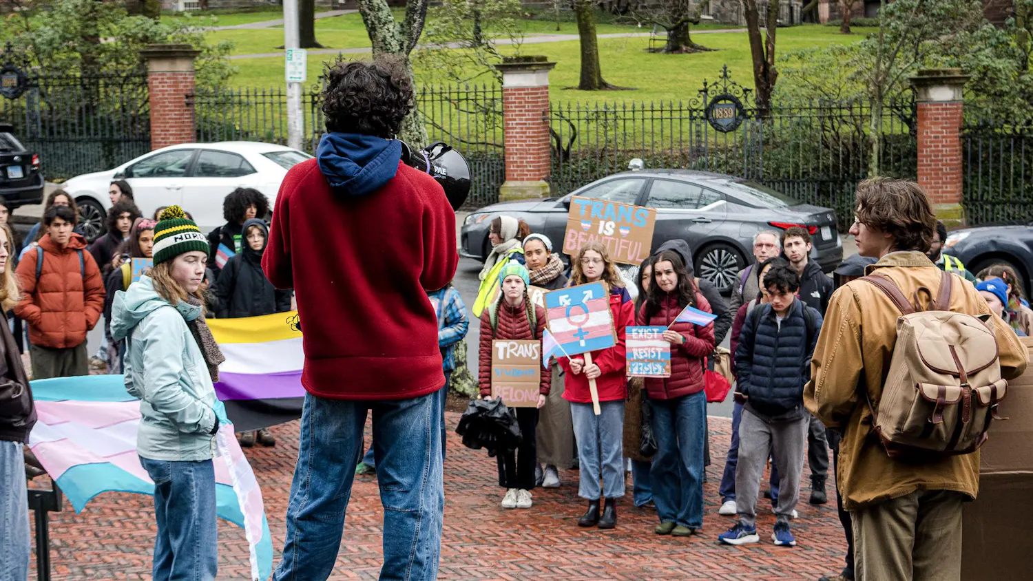 A photo of a trans rights protestor rallying in front of a crowd at the John D. Rockefeller Library.