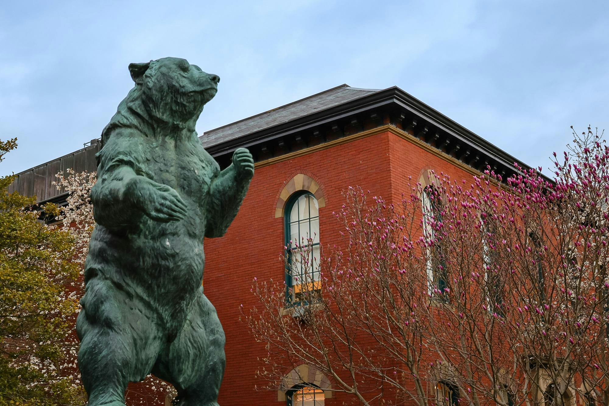 A photo of the bronze Bruno statue on the Main Green with flowers blooming in the background.