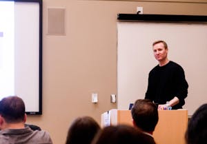 Photo of Will Dobbie at a wooden stand giving a lecture to a group of students.