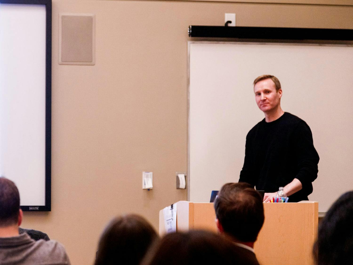 Photo of Will Dobbie at a wooden stand giving a lecture to a group of students.