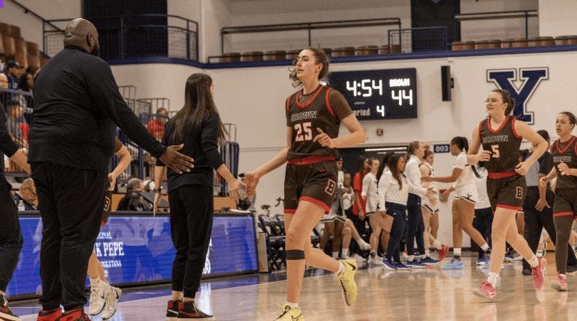 An image of player 25 of Brown's women basketball team high-fiving the coaches.
