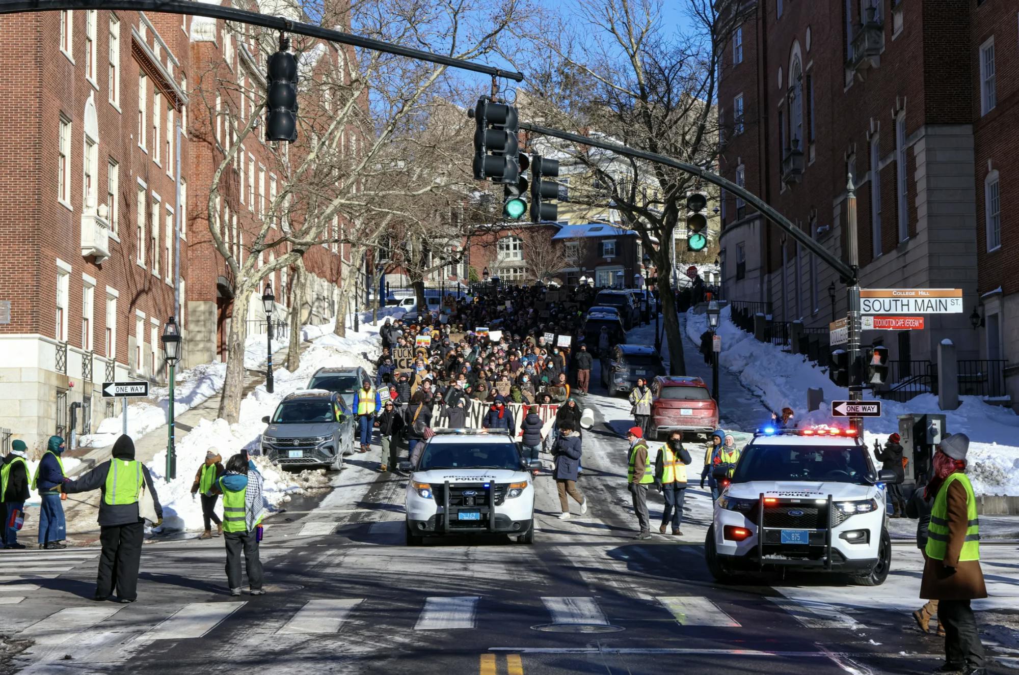 Photo of a group of protestors walk down a hill, following a Providence Police Department vehicle.