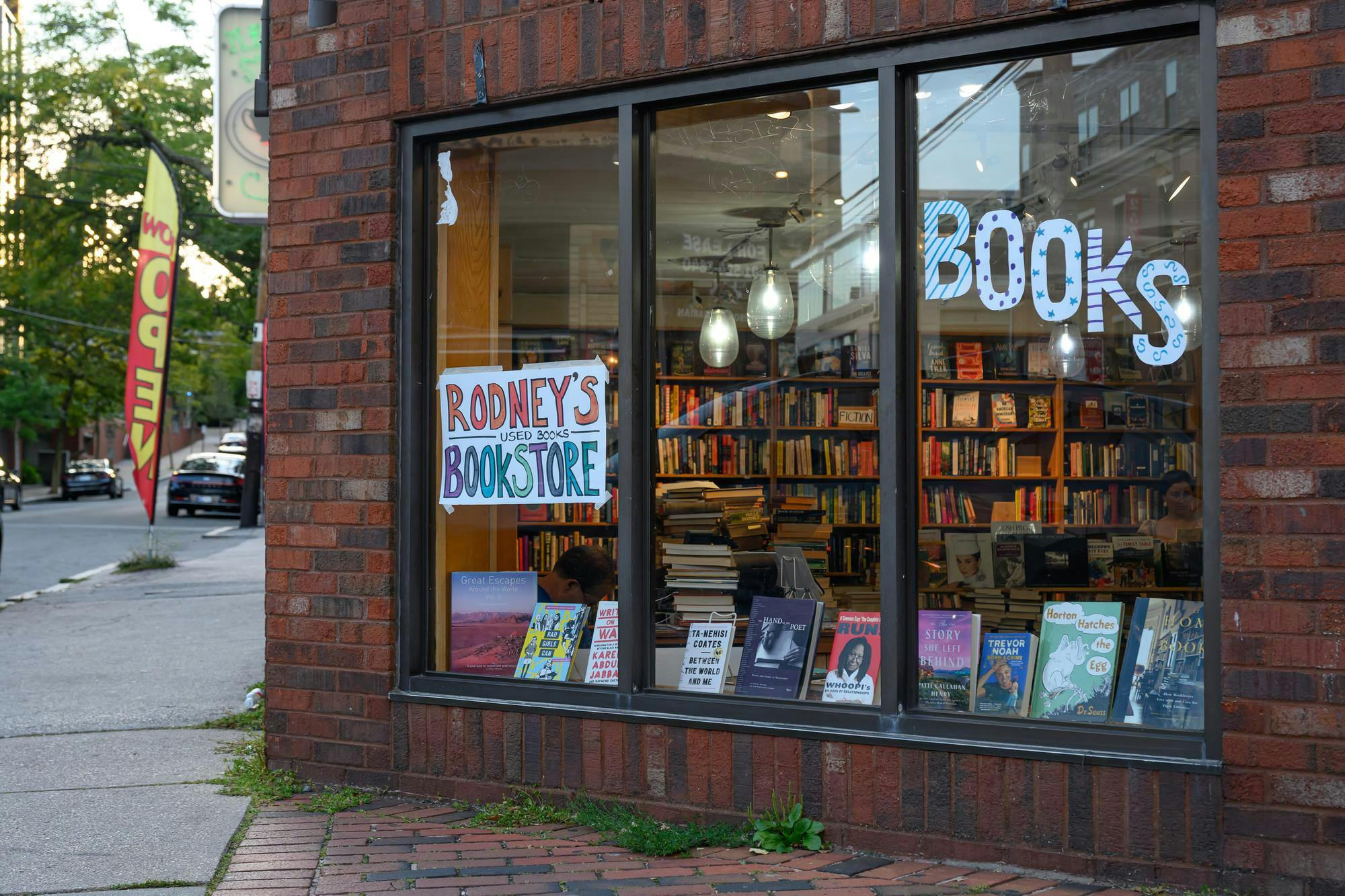 A photo of the brick exterior of Rodeny’s bookstore. Bookshelves are visible through a large window.