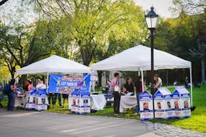 Blue and white display on a green field titled with a blue banner saying "Let Them Go Now". The display is made up of two white tents and tables. In front of the tables are multiple large cardboard signs emulating milk cartons with kidnapping victims. 