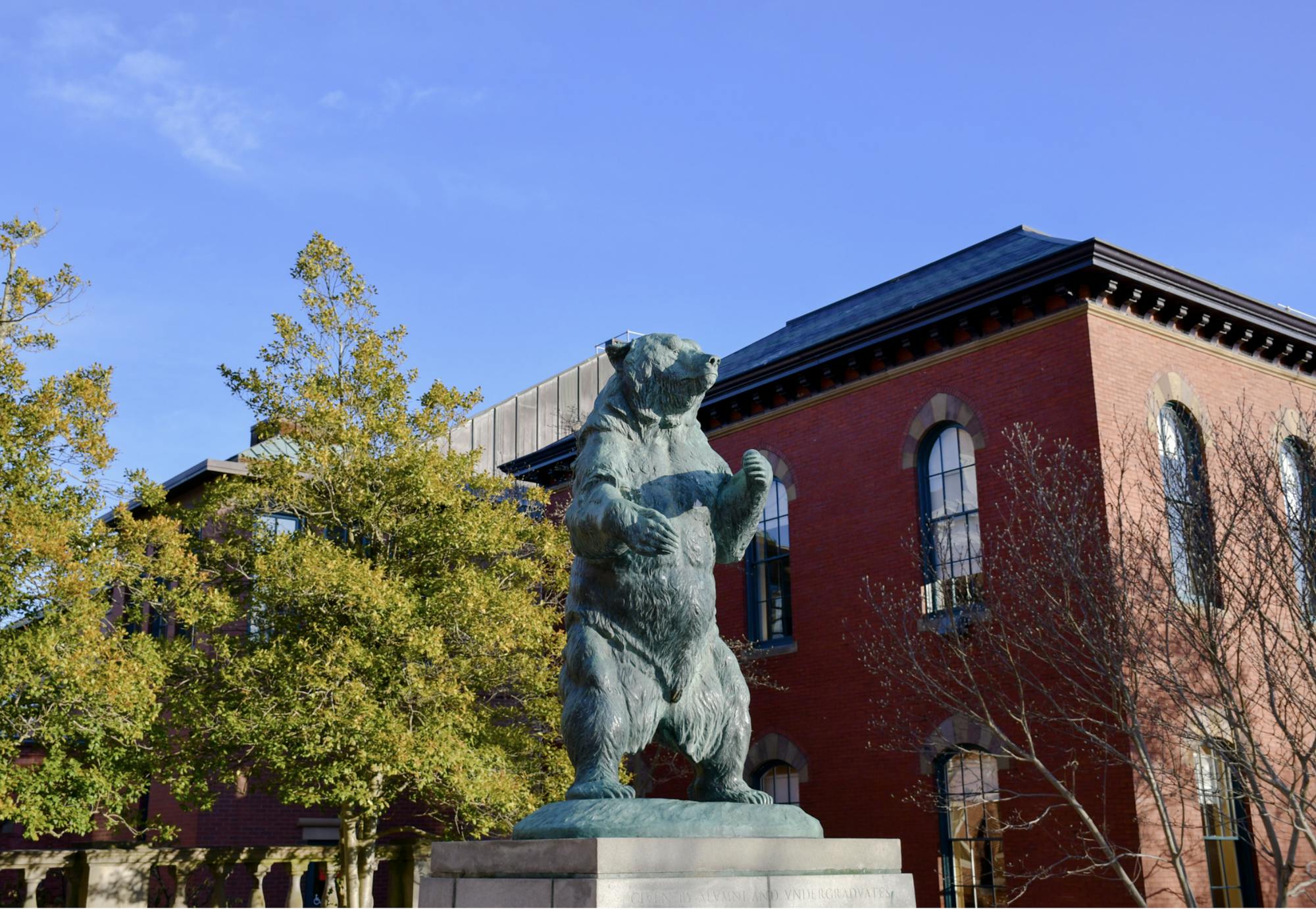 A green bear statue stands near a brick building on Brown's Main Green.