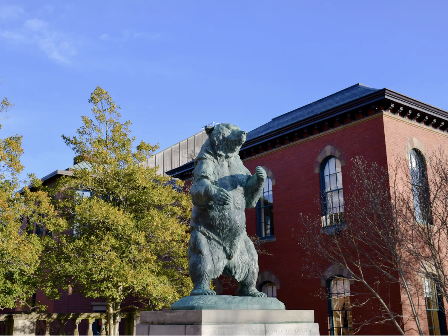A green bear statue stands near a brick building on Brown's Main Green.