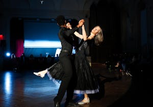A man in all black dips a woman in a black dress in a ballroom.