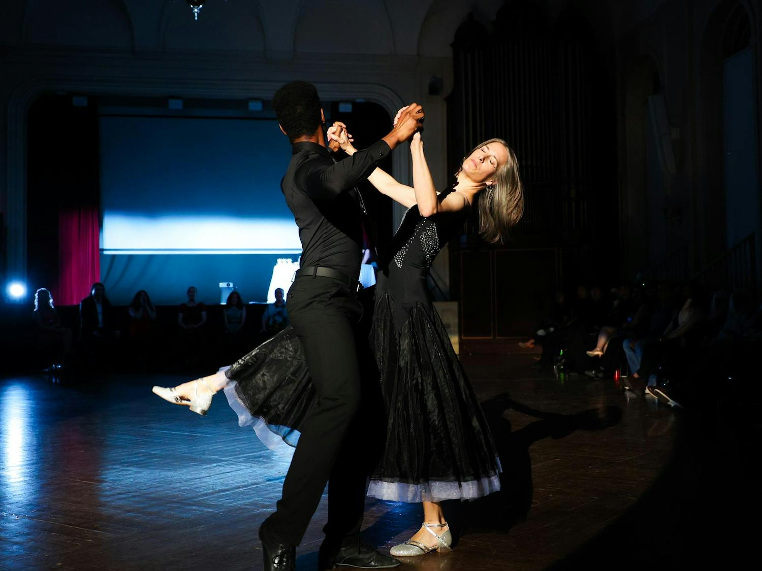 A man in all black dips a woman in a black dress in a ballroom.