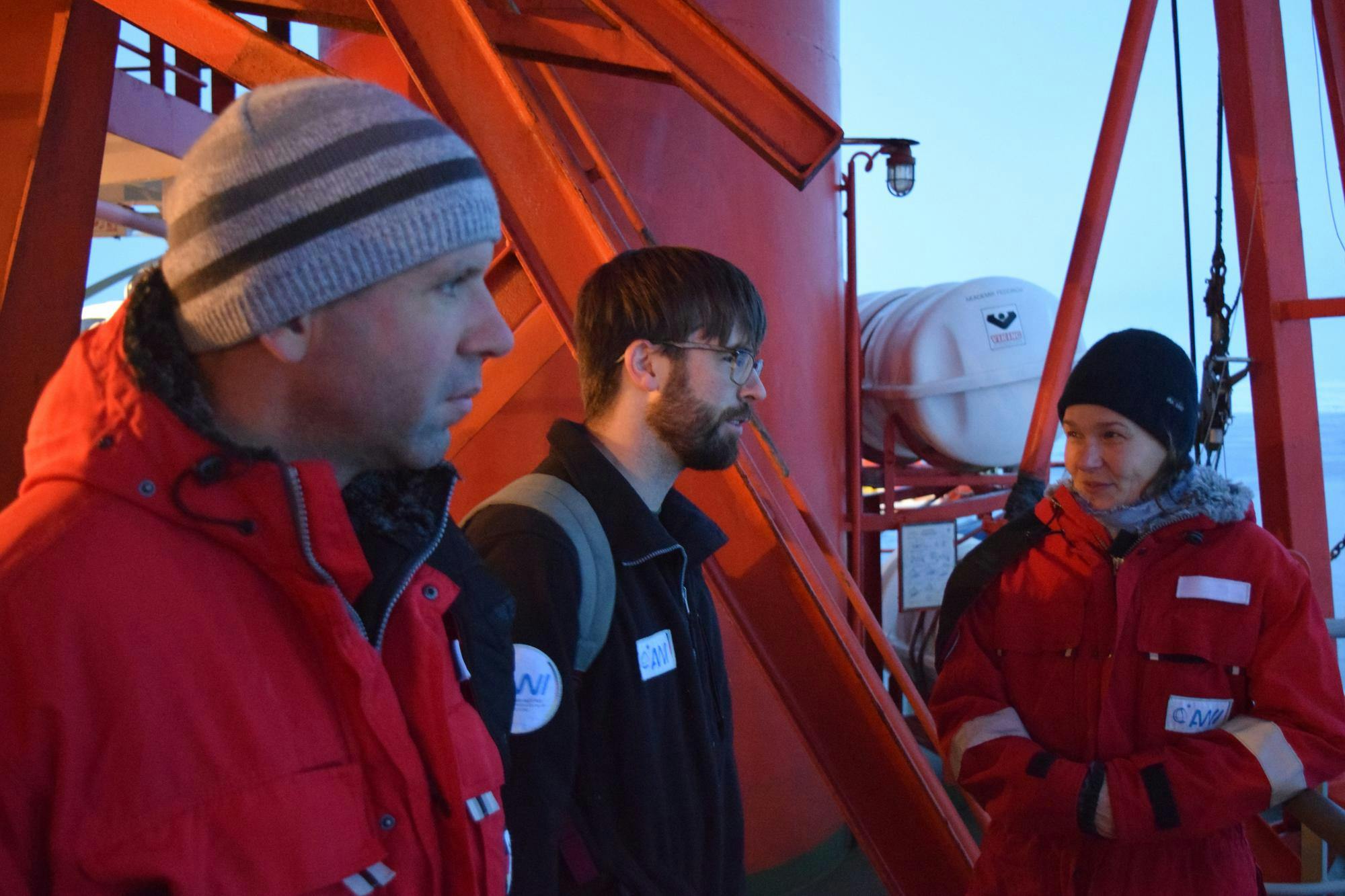 Photo of three researchers in snowsuits chatting on a boat.