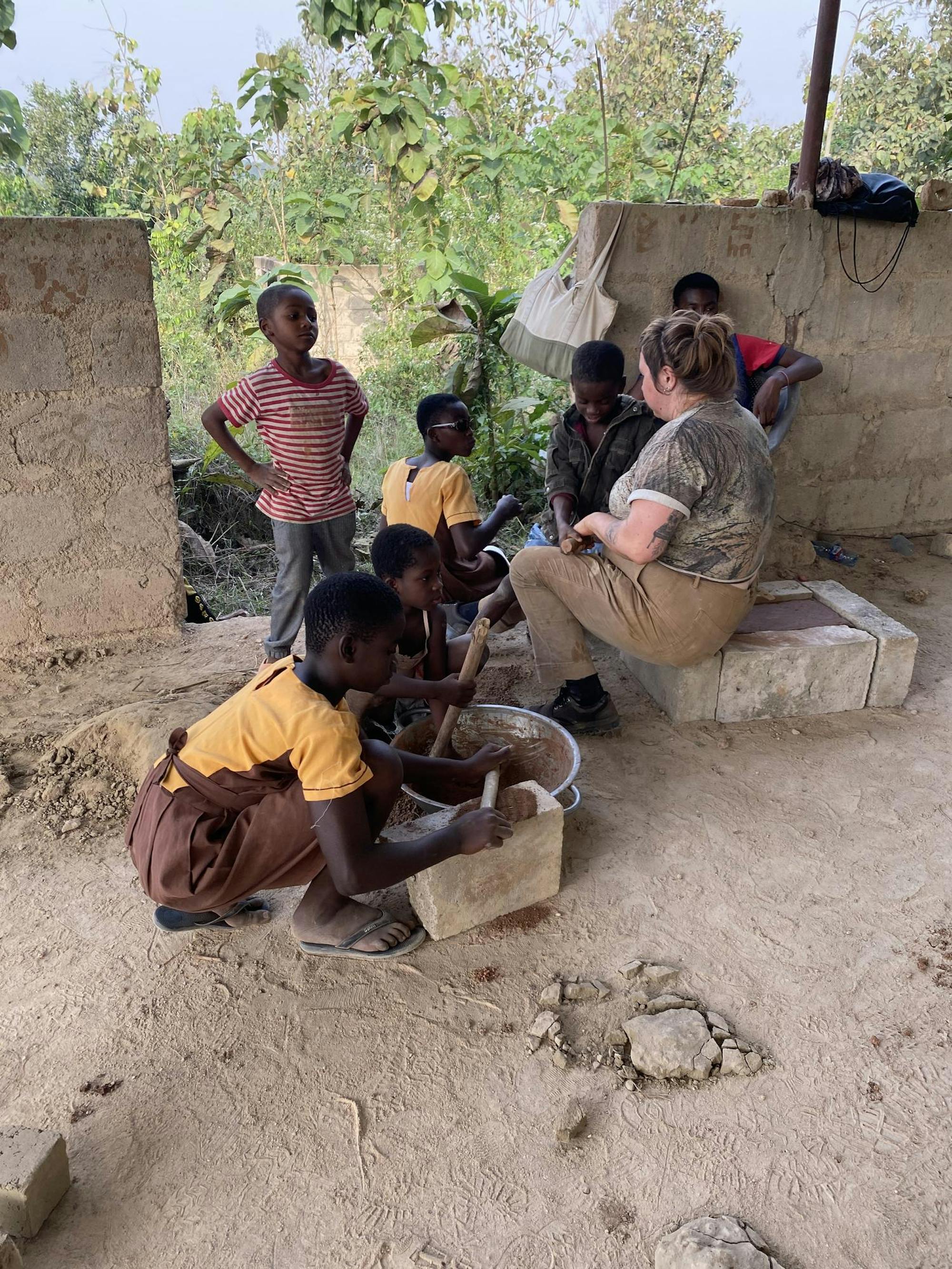 Photo of children squatting on the floor, rolling out clay and mixing clay with water.