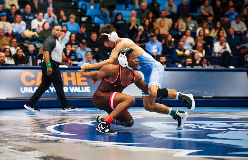 Photo of a male wrestler from Brown University attempting to lift a Columbia opponent wearing light blue during a wrestling match.