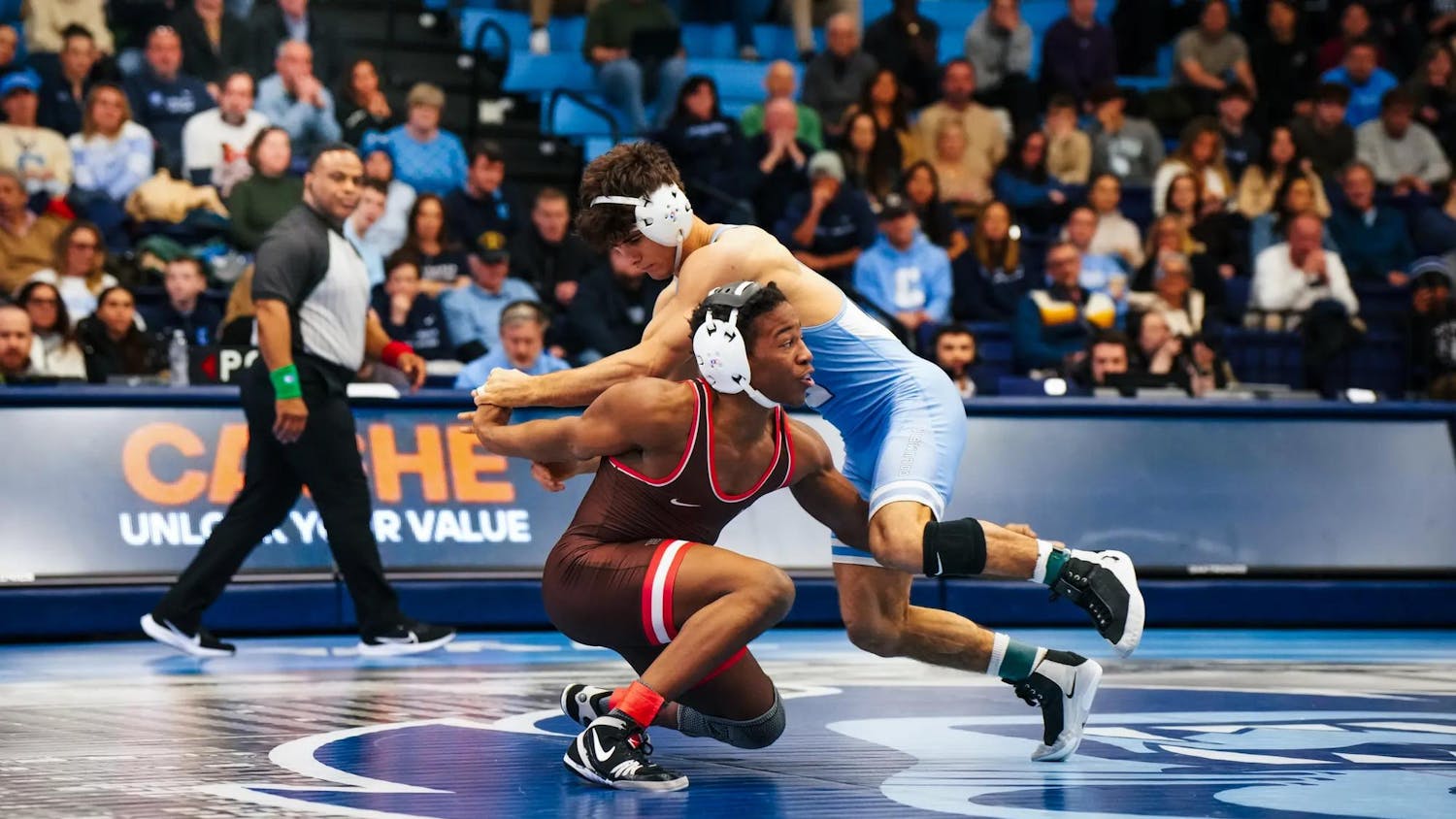 Photo of a male wrestler from Brown University attempting to lift a Columbia opponent wearing light blue during a wrestling match.