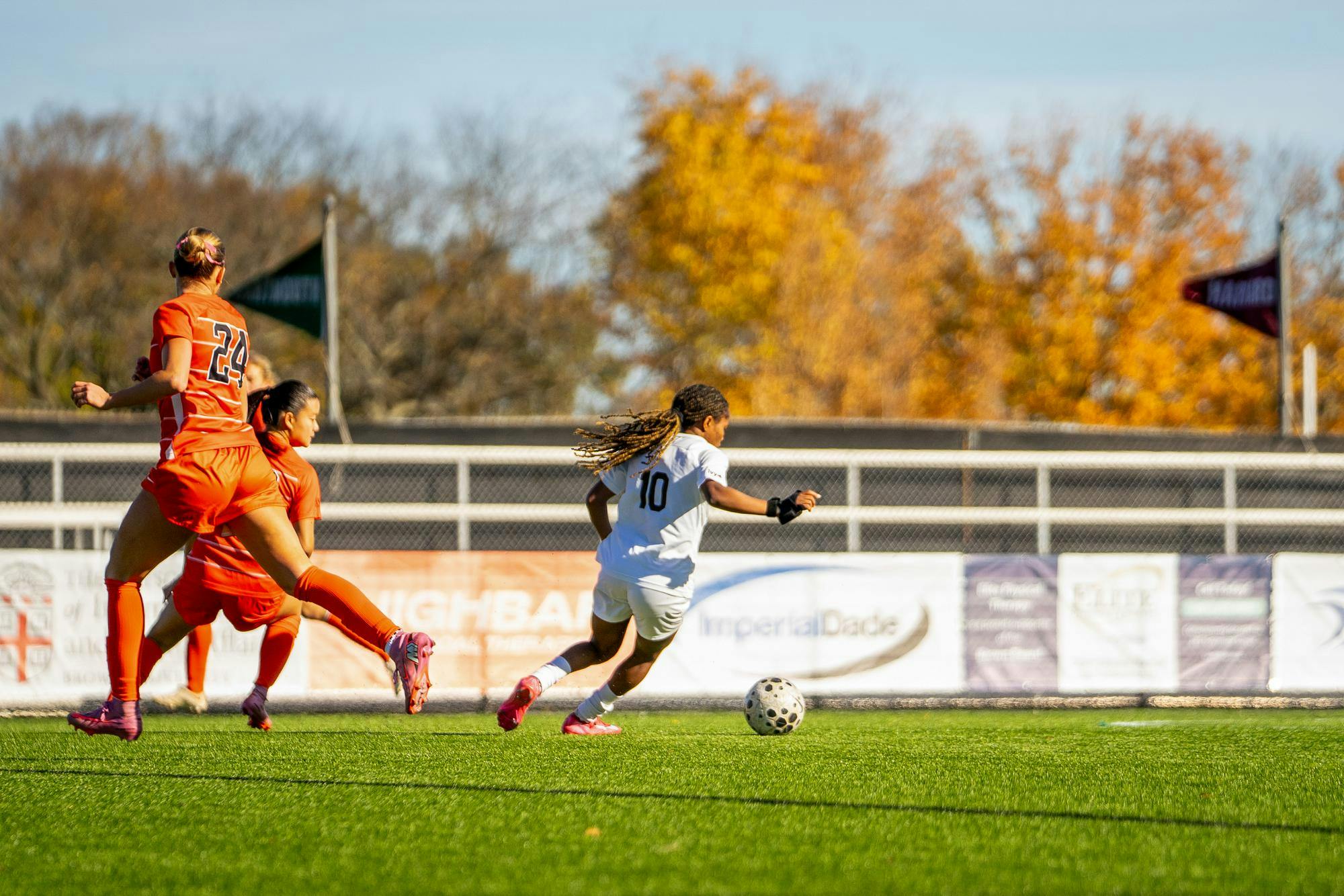 Photo of a soccer player in a white jersey dribbling the ball downfield.